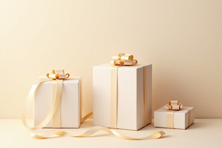 Drei in hellen Beige- und Cremetönen verpackte Geschenke mit eleganten Schleifen vor einem minimalistischen, beigefarbenen Hintergrund.